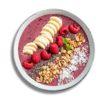 A smoothie bowl topped with sliced bananas, raspberries, granola, chia seeds, shredded coconut, and a small mint leaf.